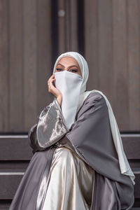 Portrait of a veiled woman with white niqab sitting on the stairs in front of the building