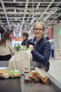 Portrait of woman holding groceries bag at checkout counter in supermarket