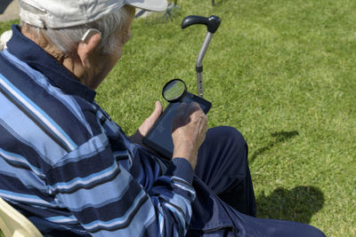 Senior man looking through magnifying glass while using mobile phone in backyard