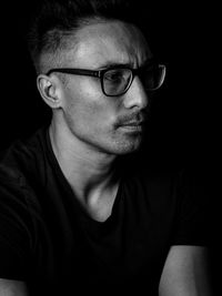 Close-up portrait of man wearing eyeglasses against black background