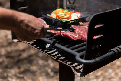 Cropped image of man preparing meat on barbeque grill at park