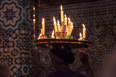 Rear view of dancer carrying tray of illuminated candles against patterned wall