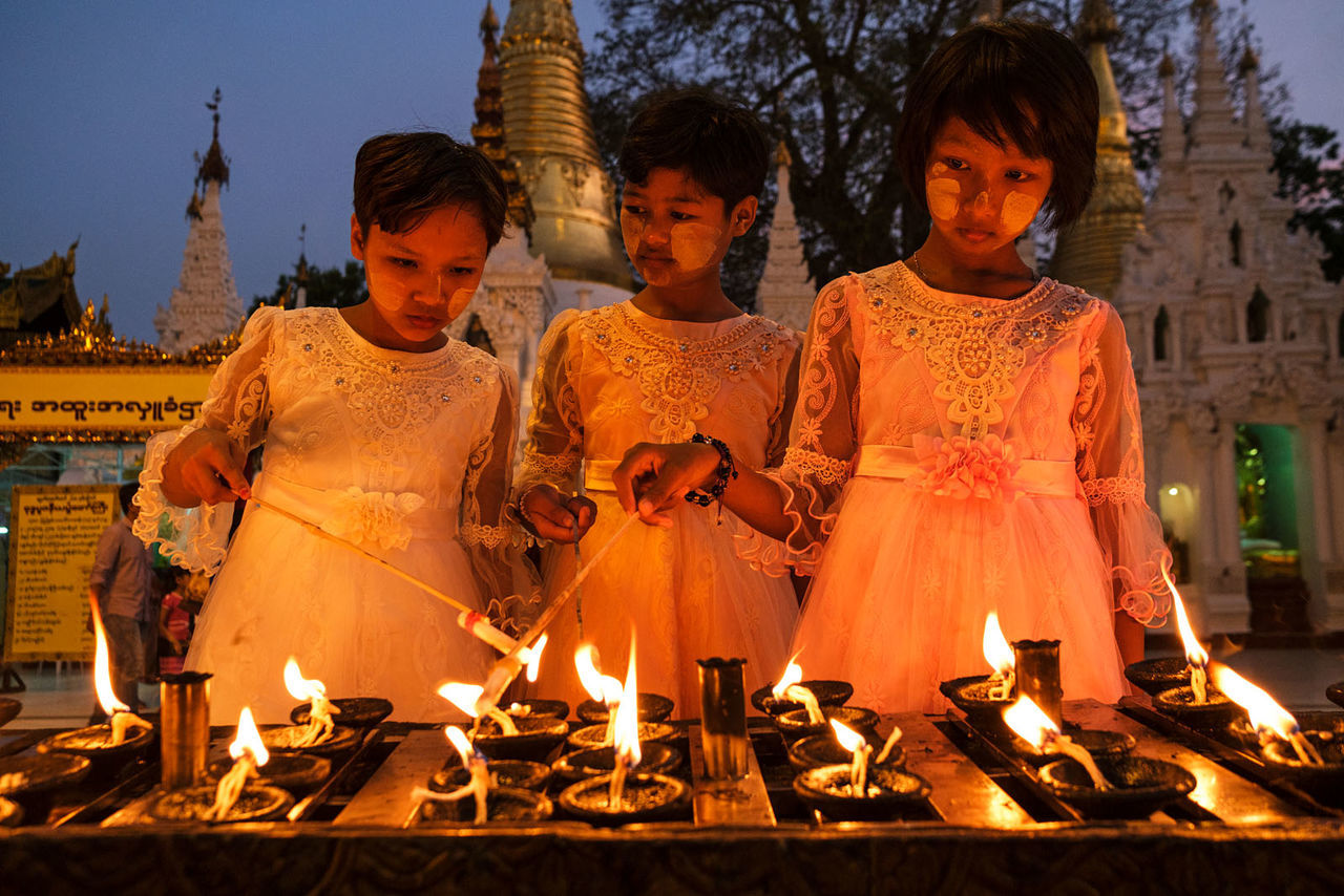 burning, flame, fire, religion, candle, adult, nature, women, belief, heat, group of people, togetherness, spirituality, men, temple, architecture, tradition, child, traditional clothing, person, clothing, event, female, smiling, temple - building, celebration, building, childhood, night, young adult, outdoors, place of worship, lifestyles, dusk, built structure, emotion