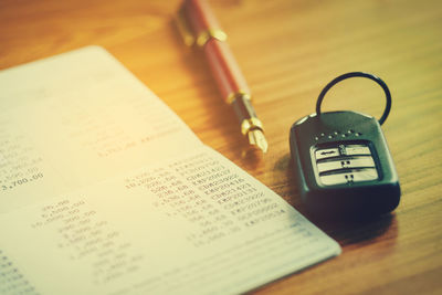 Close-up of bank book by car key and pen on table