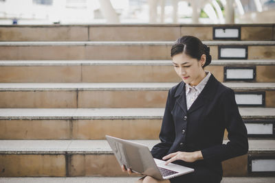 Businesswoman using laptop while sitting on steps in city