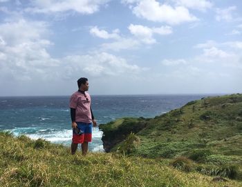 Man standing on cliff by sea against sky