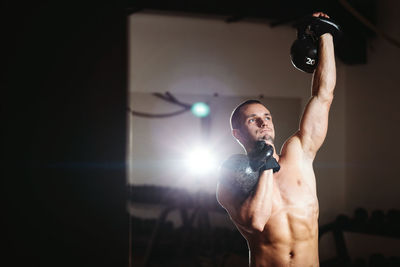 Shirtless muscular man lifting weights while standing in gym