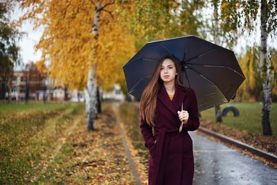 Portrait of woman with umbrella standing against trees during rainy season