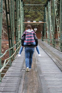 Rear view of boyfriend piggybacking girlfriend while walking on footbridge