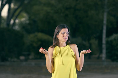 Portrait of woman gesturing while standing against trees on road