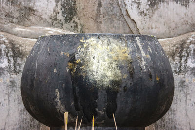 Close-up of old container on rock against wall