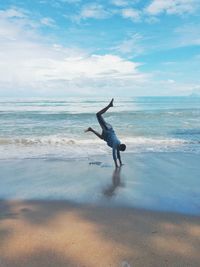 Man performing handstand on sea shore against sky