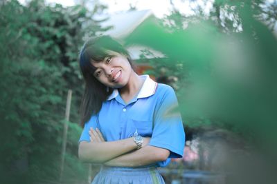 Portrait of smiling young woman standing against trees