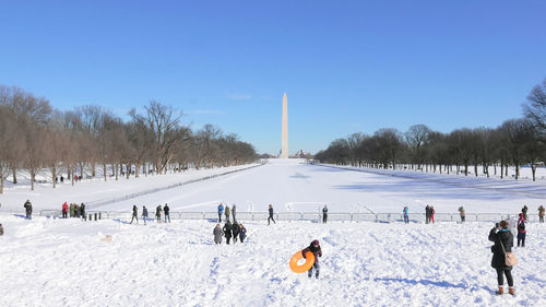 People playing in the snow in front of the washington monument against clear blue sky