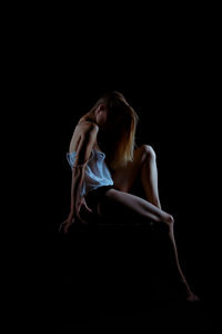 Young woman sitting against black background