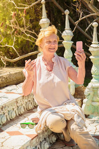 Mature woman traveler sitting on steps and using mobile phone