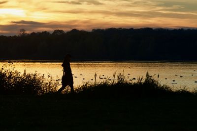 Silhouette woman standing by lake against sky during sunset