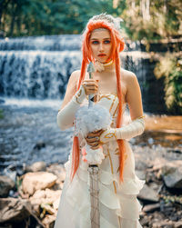 Portrait of young woman standing against waterfall