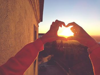 Close-up of hands holding heart shape against sky during sunset
