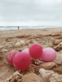 Pink balloons on sand at beach against sky