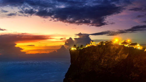 Uluwatu temple on cliff by sea against sky during sunset