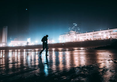 Silhouette man standing on illuminated street at night