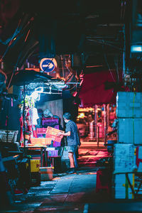 Rear view of woman standing on illuminated street at night