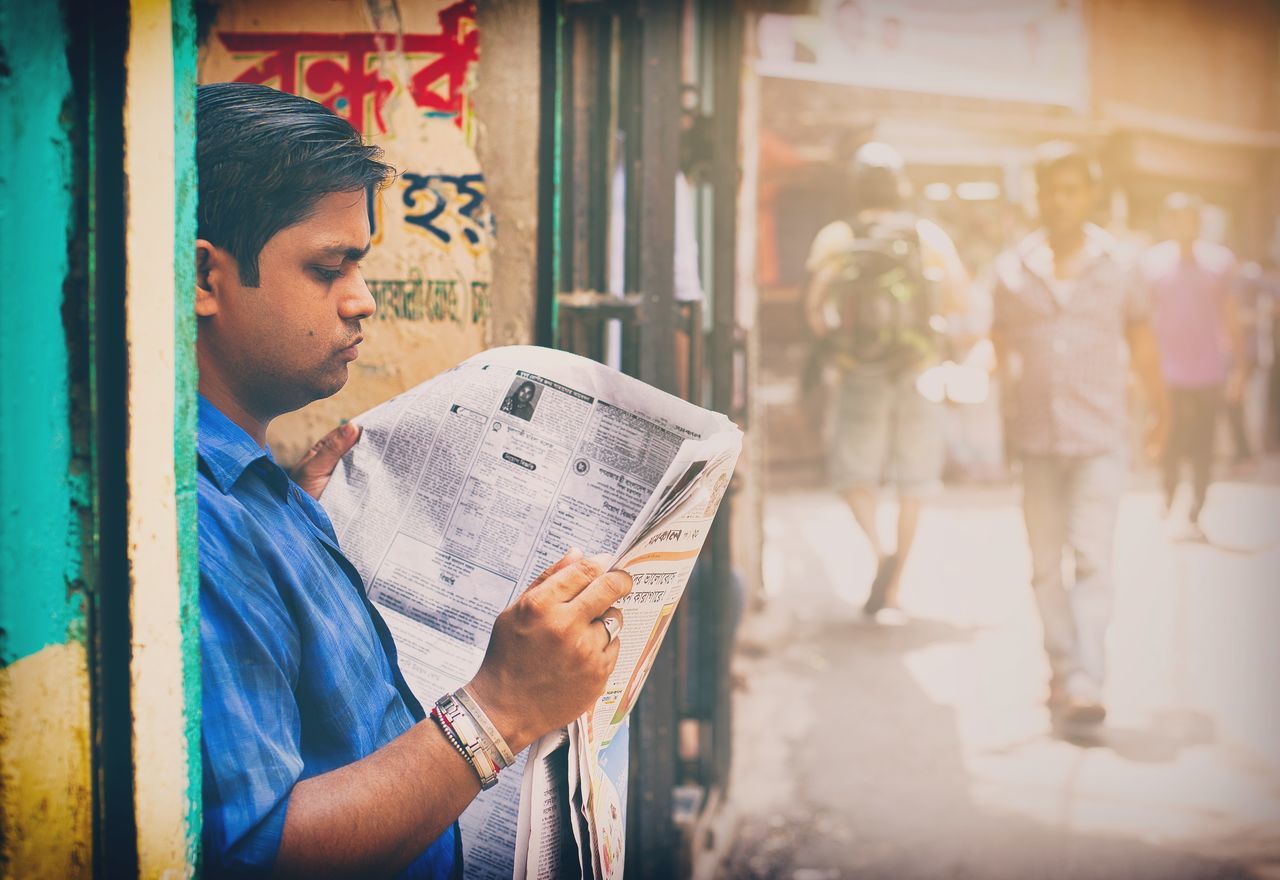 YOUNG MAN LOOKING AWAY WHILE HOLDING PAPER AT ENTRANCE