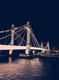 Illuminated suspension bridge over river against sky at night