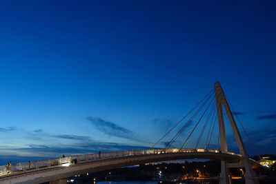 Bridge over illuminated city against blue sky