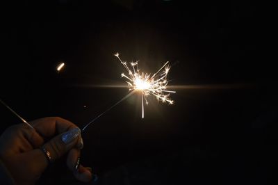 Cropped hand of woman holding illuminated sparkler at night