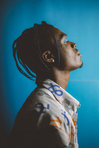 Serious african american male with braided hairstyle and bright makeup looking away on blue background in studio