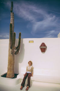 Woman sitting on seat by saguaro cactus against wall