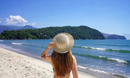 Rear view of woman standing at beach against sky