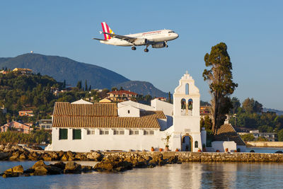 Airplane flying over buildings by mountains against sky