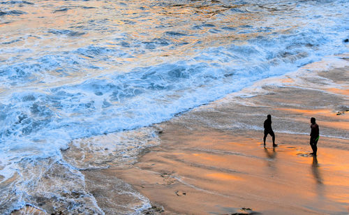 Silhouette friends standing on shore at beach