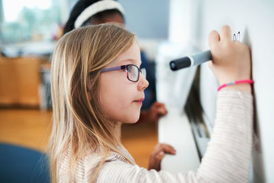 Close-up of girl wearing eyeglasses writing on whiteboard in classroom