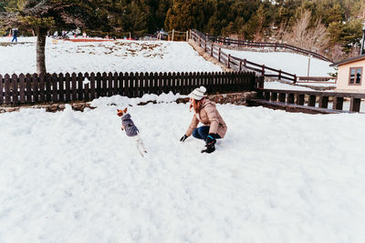 Woman playing with dog on snow covered field