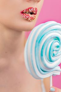 Close-up of woman holding blue lollipop against pink background