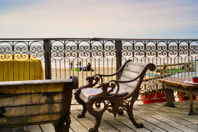 Empty chairs and table against railing by sea against sky