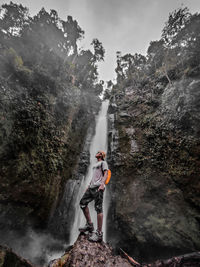 Man standing on rock against waterfall