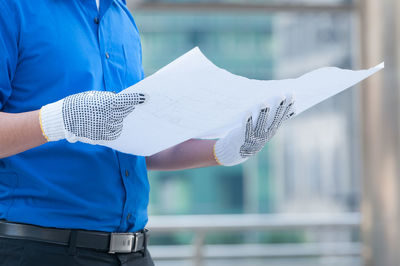 Midsection of man holding paper while standing against blue background