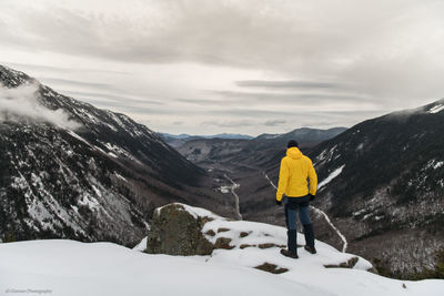 Rear view of person walking on snowcapped mountains against sky