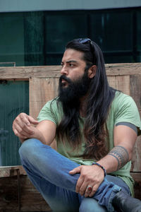 Man looking away while sitting on wood