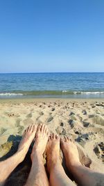 Low section of people on beach against clear sky