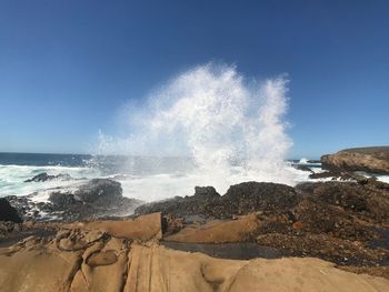 Panoramic view of waves breaking on beach against clear sky