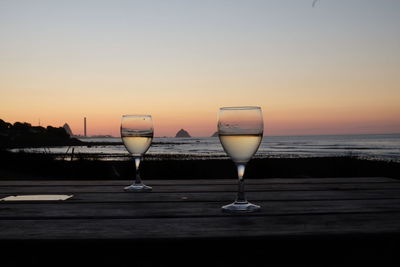 Wineglass on beach against clear sky during sunset