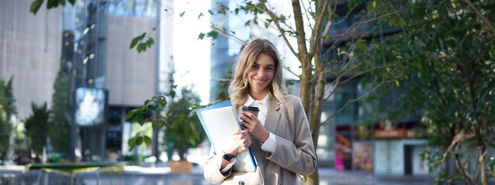 Portrait of young woman standing against building