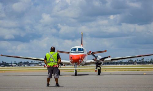 Man standing on airplane at airport runway against sky