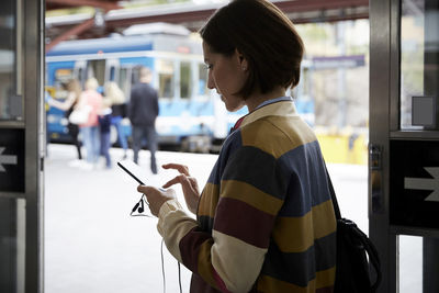 Businesswoman using smart phone while standing in railroad station